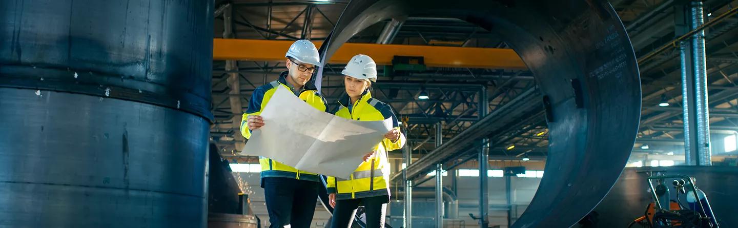 Two construction workers reviewing plans in a large warehouse