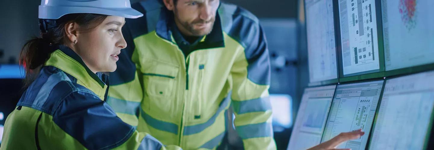 Two people in high visibility and hats looking at screens