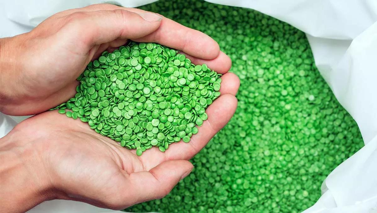 Hände, die grüne Plastikpellets halten