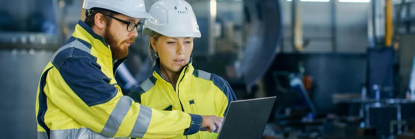 Two factory workers looking at tablet with hardhats