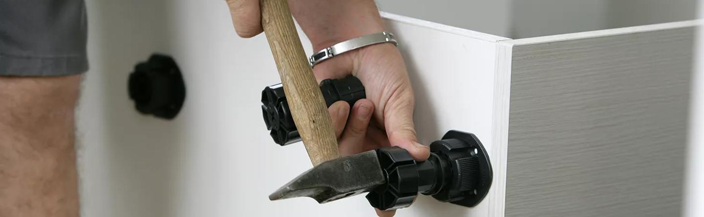 furniture maker hammering feet into cabinet